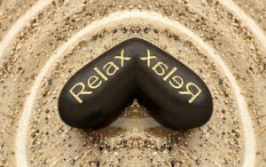 stein im sand mit der aufschrift RELAX - alexander-technik-mg